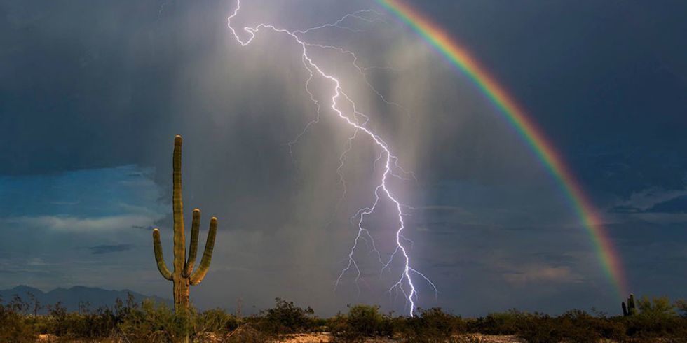 an incredibly rare and well-timed shot of lightning striking the sky next to a rainbow